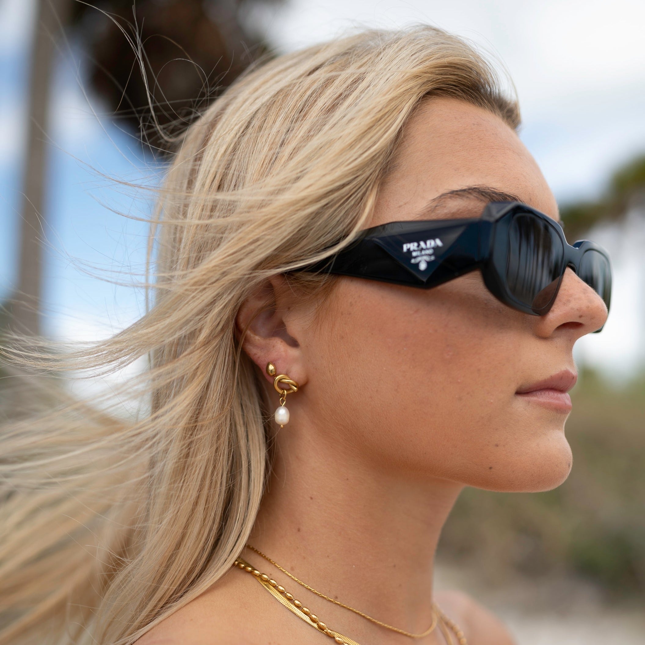 Woman wearing Prada sunglasses with a blurred natural background
